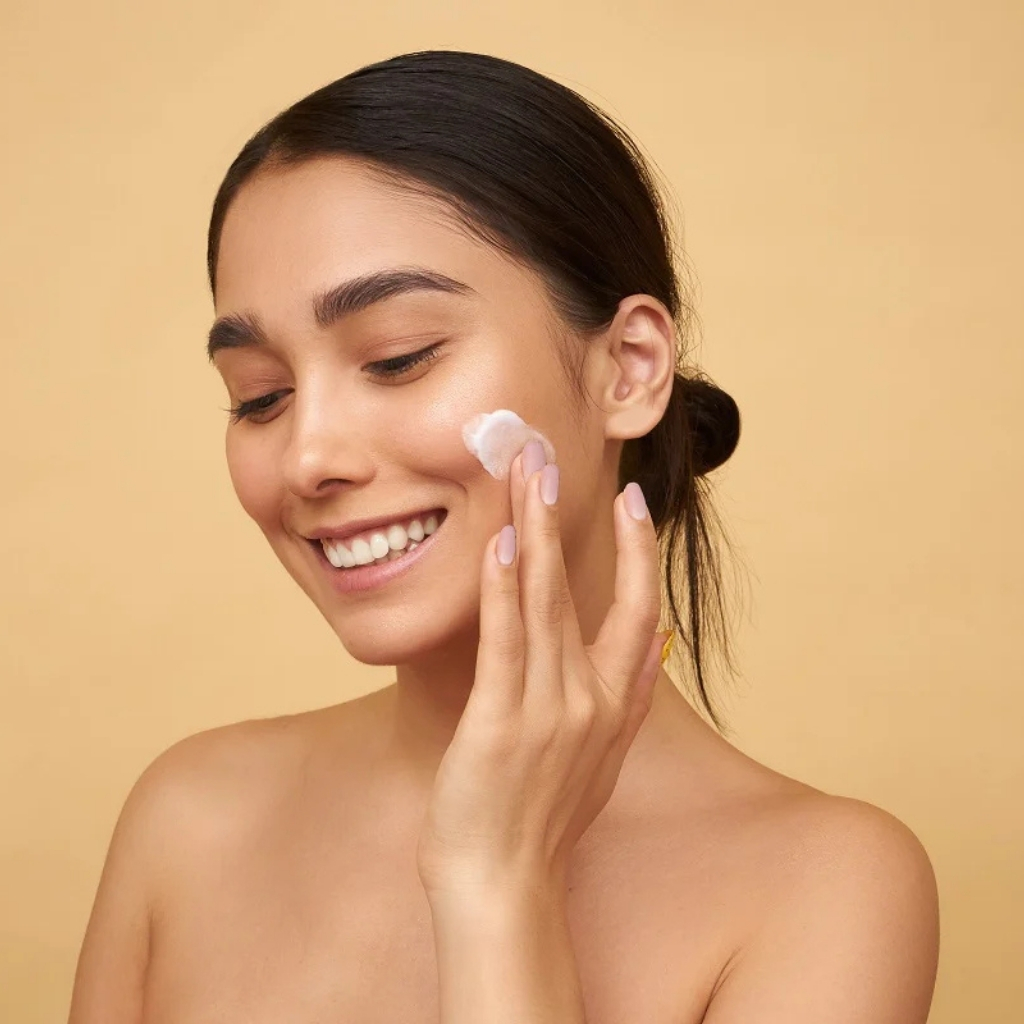 Smiling woman with radiant skin applying herbal moisturizer.